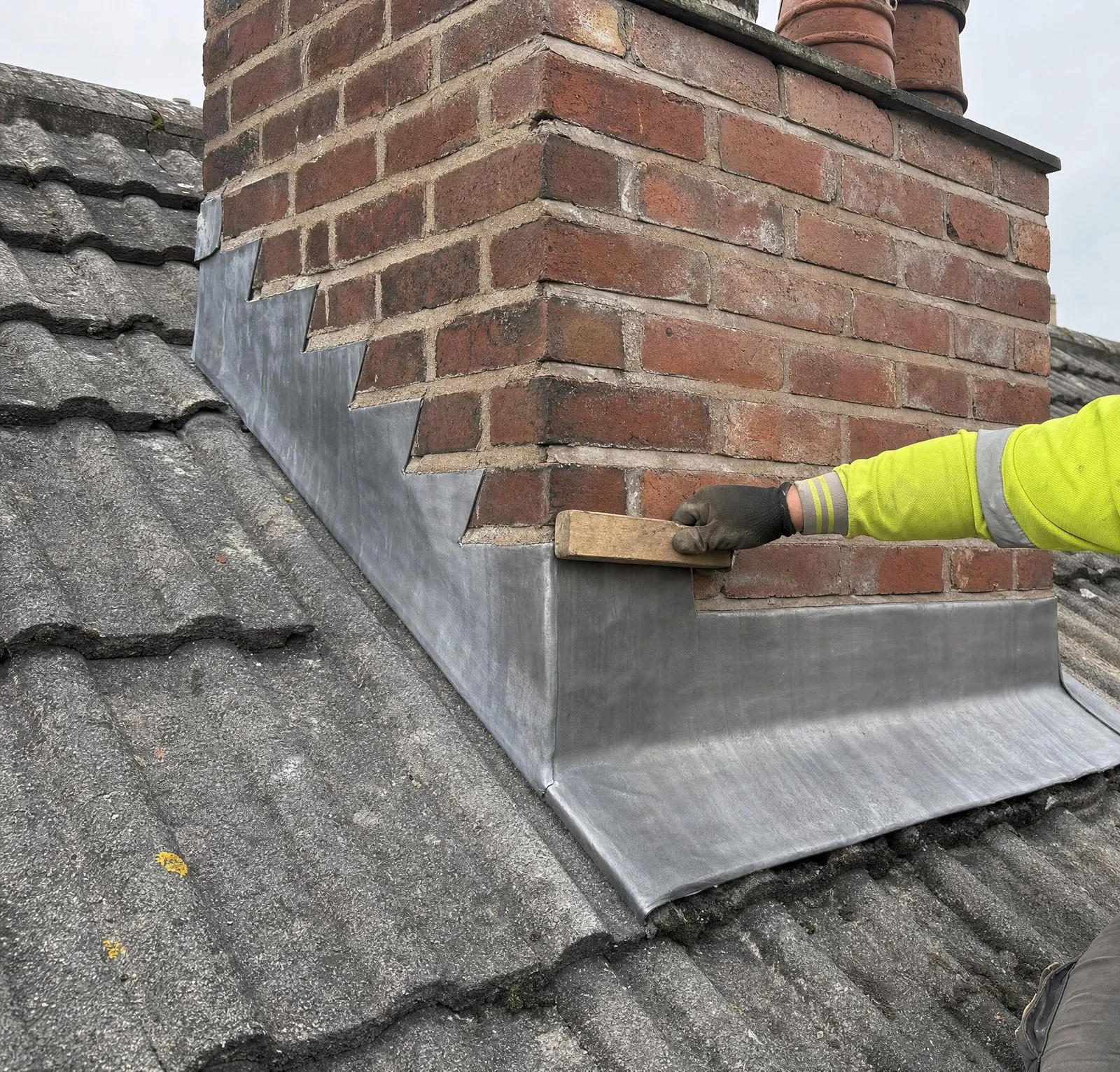 New stepped lead flashing being dressed into the mortar joints of a chimney stack
