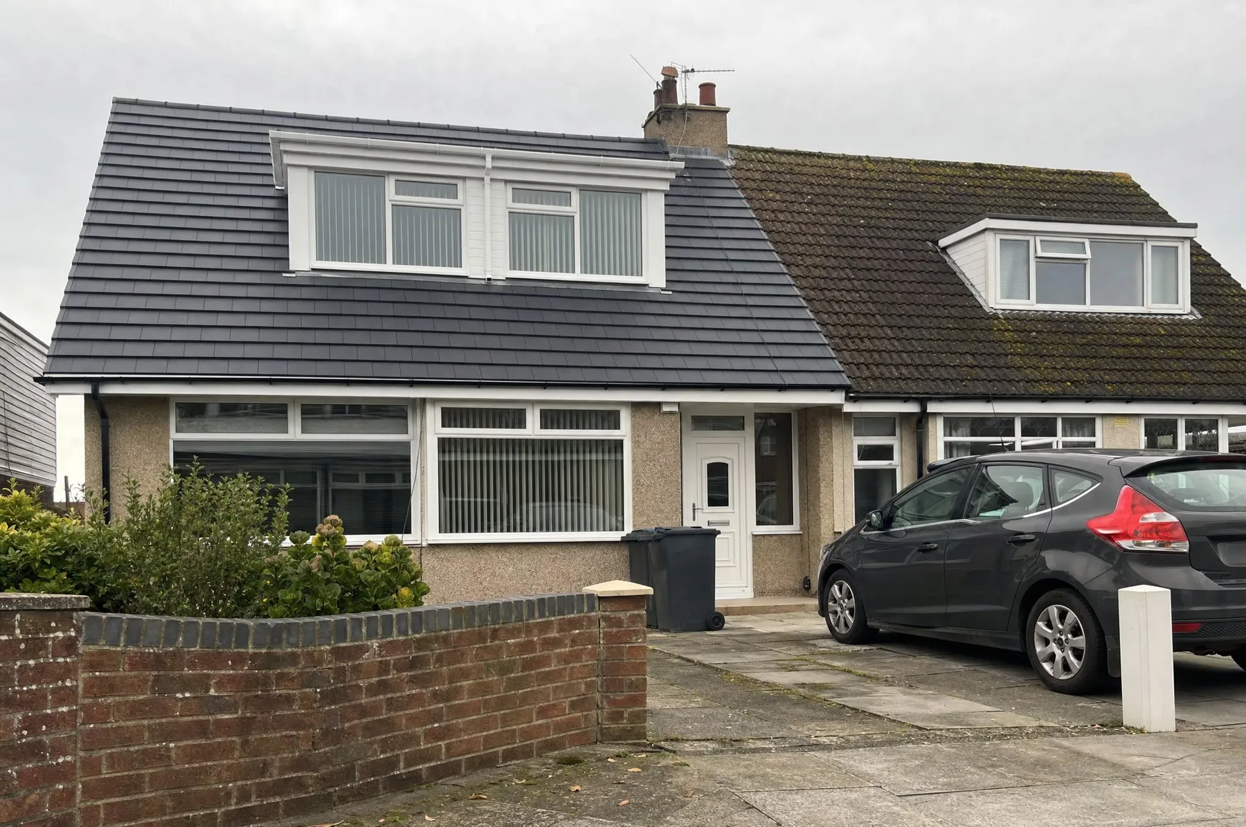 A finished re-roof in new grey concrete tiles on a dormer bungalow, next to the old mossy roof next door