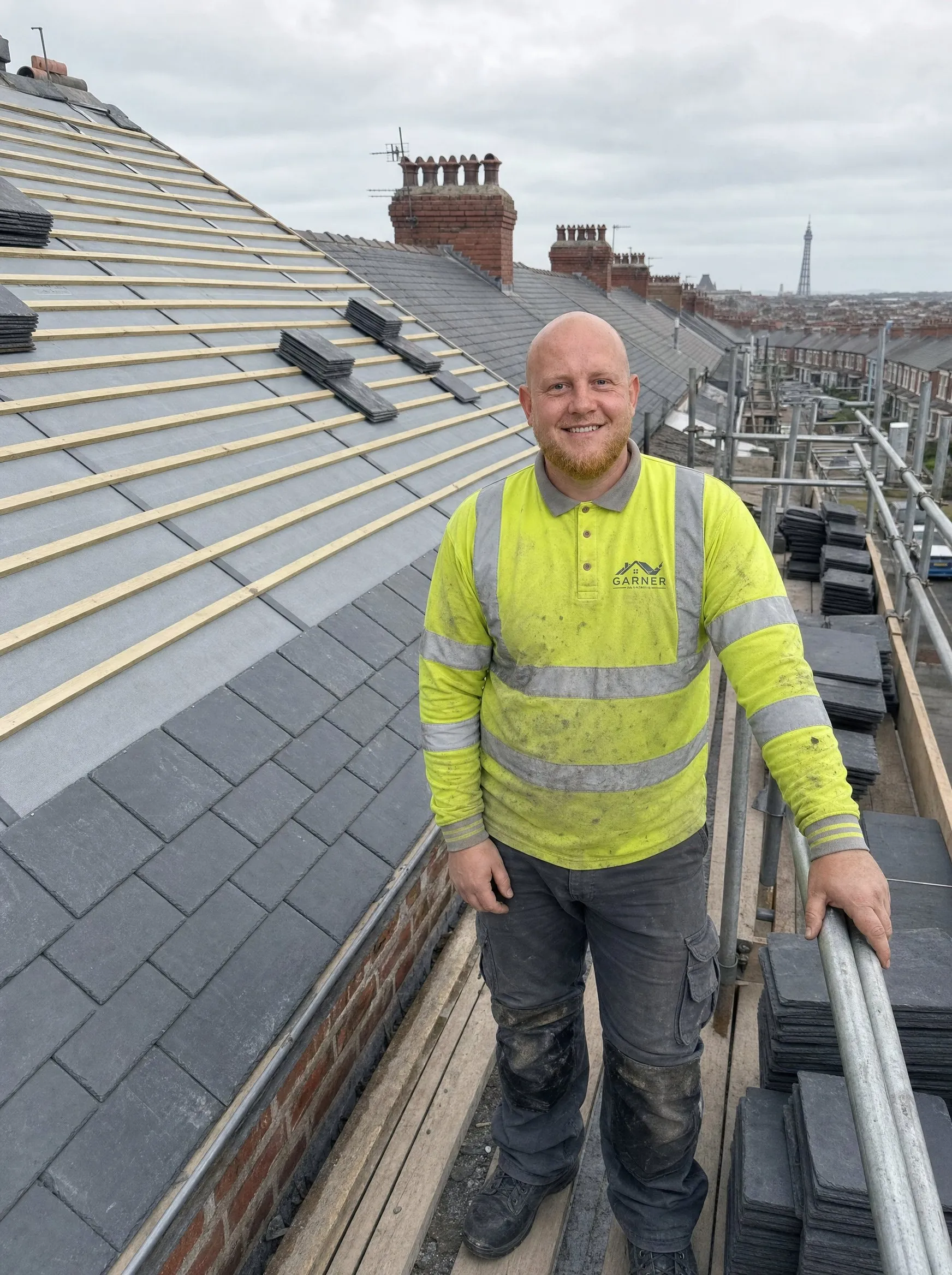 Jamie Garner on the scaffold of a slate re-roof in Blackpool, with Blackpool Tower on the skyline